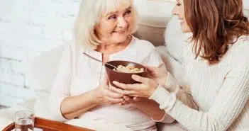 Une femme qui sert une petit déjeuner à une personne agée